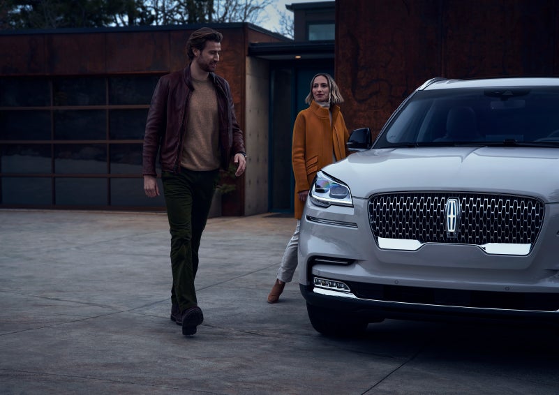 A man and a woman approaching a 2024 Lincoln Aviator® SUV, which illuminates certain lights when they are close | Parkway Lincoln in Winston Salem NC