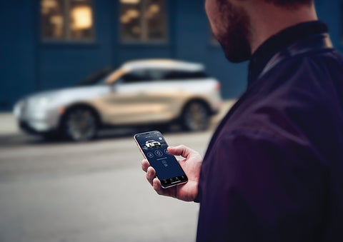 A person is shown interacting with a smartphone to connect to a Lincoln vehicle across the street. | Parkway Lincoln in Winston Salem NC