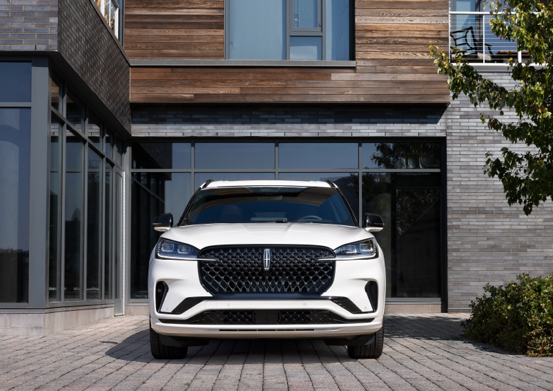 A white 2025 Lincoln Aviator® SUV is shown parked outside a modern building with gray brick and wood accents. | Parkway Lincoln in Winston Salem NC
