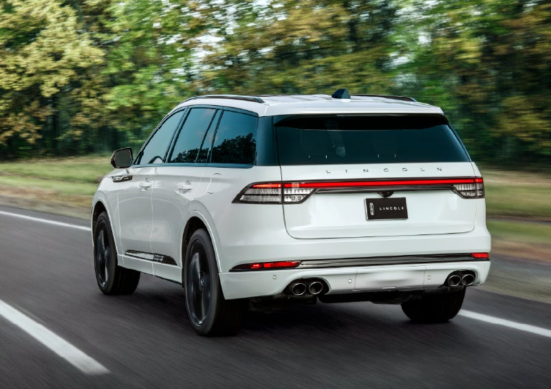 A white 2026 Lincoln Aviator® SUV is being driven away down a road lined with colorful trees. | Parkway Lincoln in Winston Salem NC