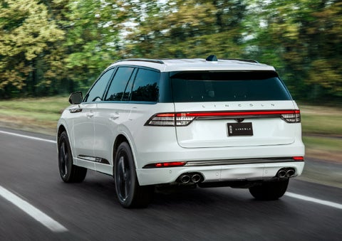 A white 2026 Lincoln Aviator® SUV is being driven away down a road lined with colorful trees. | Parkway Lincoln in Winston Salem NC