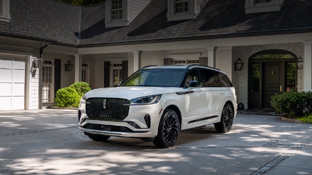 A white 2026 Lincoln Aviator® SUV is parked in the driveway of a luxury home. | Parkway Lincoln in Winston Salem NC