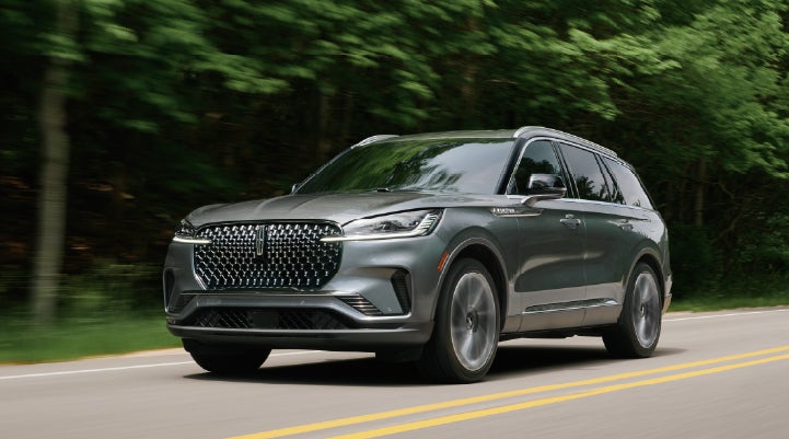 A 2027 Lincoln Aviator® SUV is being driven down a road lined with trees. | Parkway Lincoln in Winston Salem NC