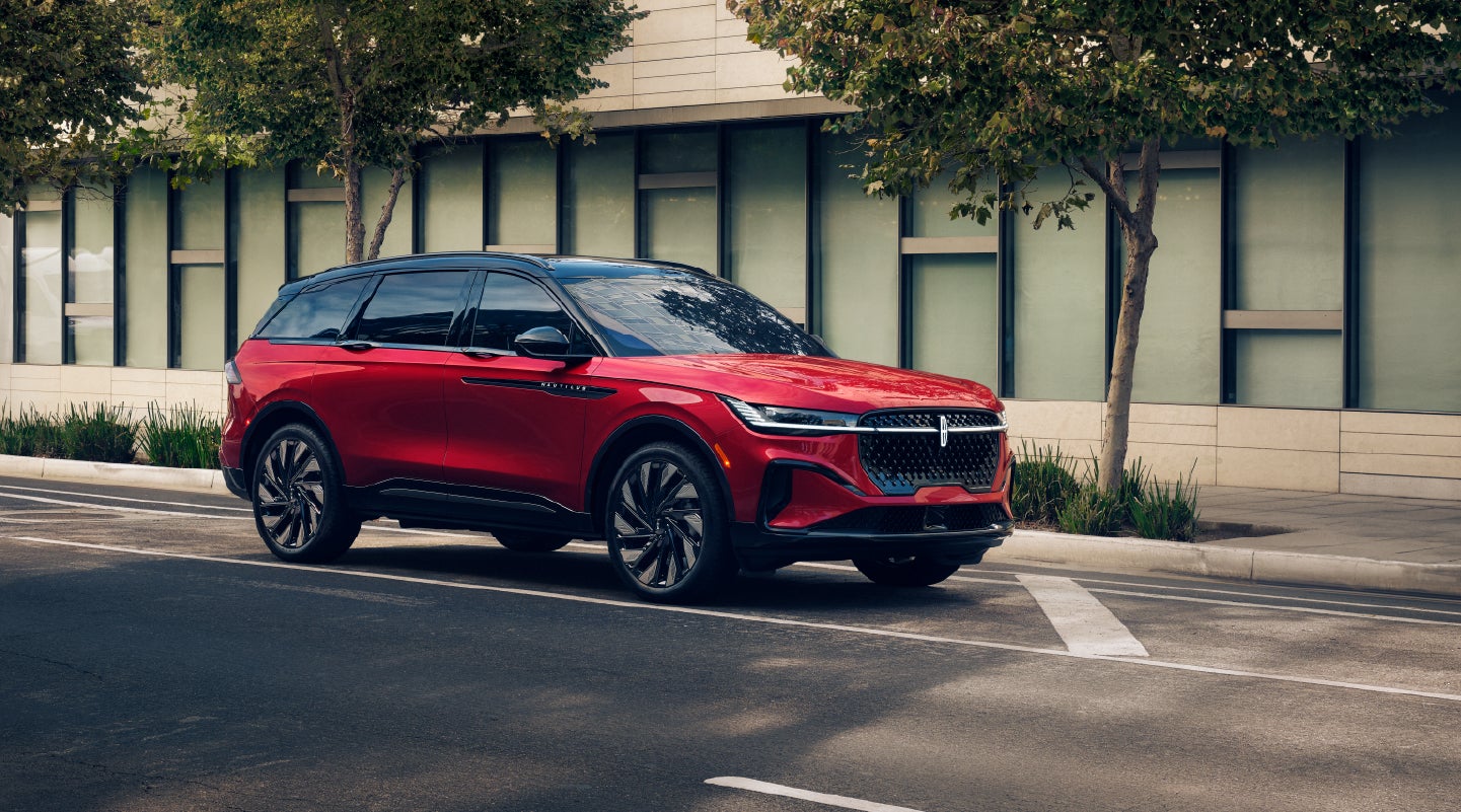 A 2026 Lincoln Nautilus® SUV driving through a modern city street lined with glass office buildings.