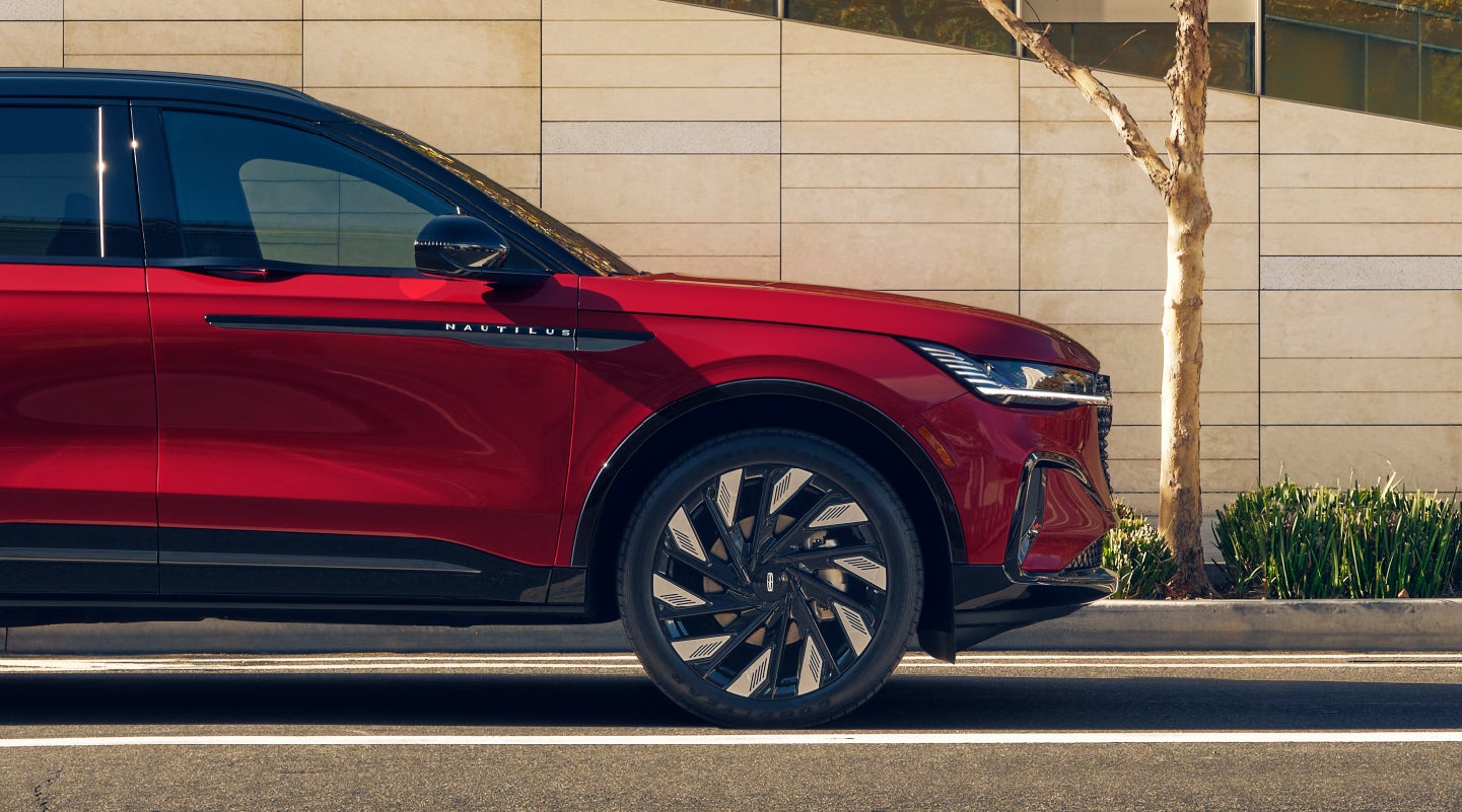 The side profile of a 2026 Lincoln Nautilus® SUV parked along a tree-lined urban street in front of contemporary architecture.